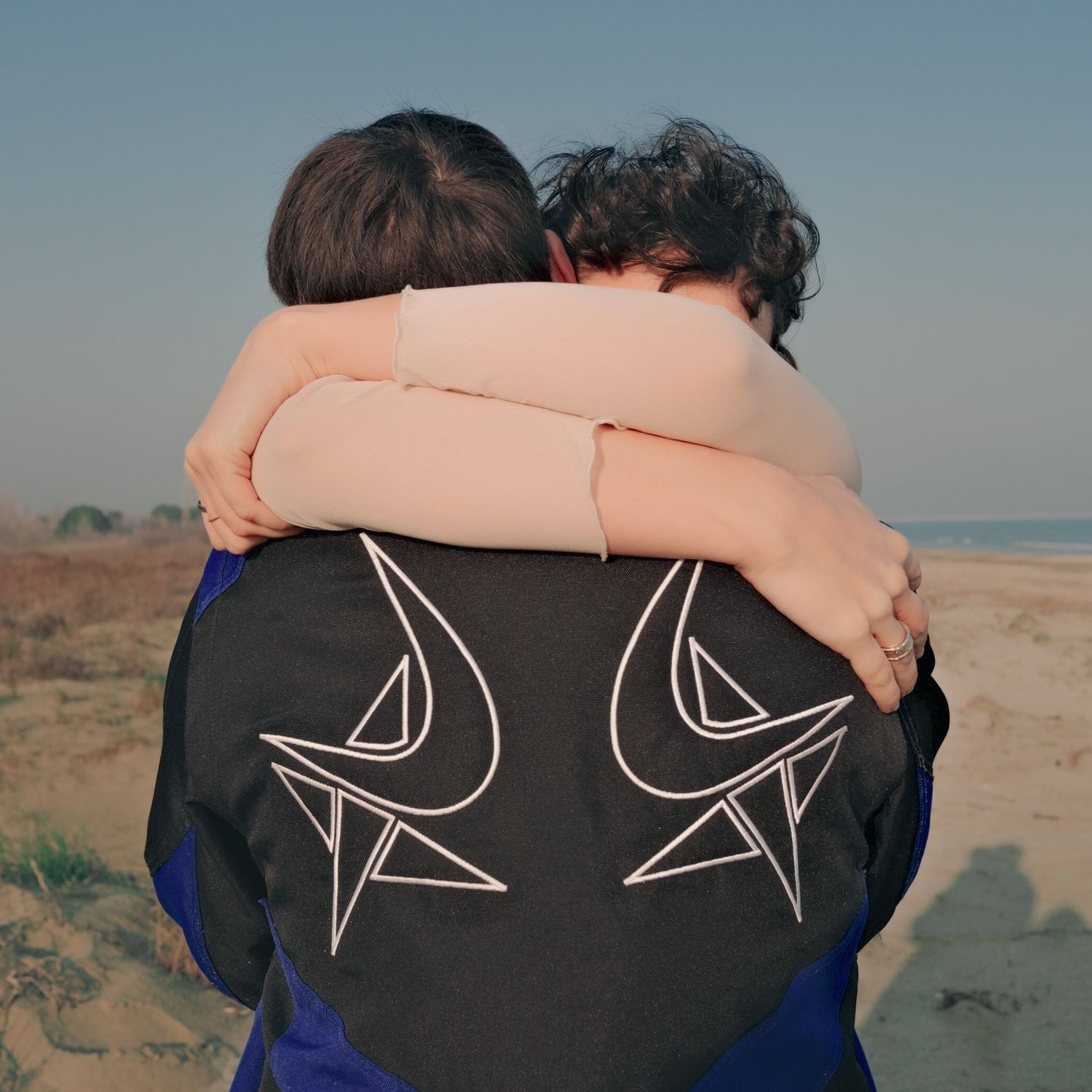 Two people hugging on a beach, seen from behind