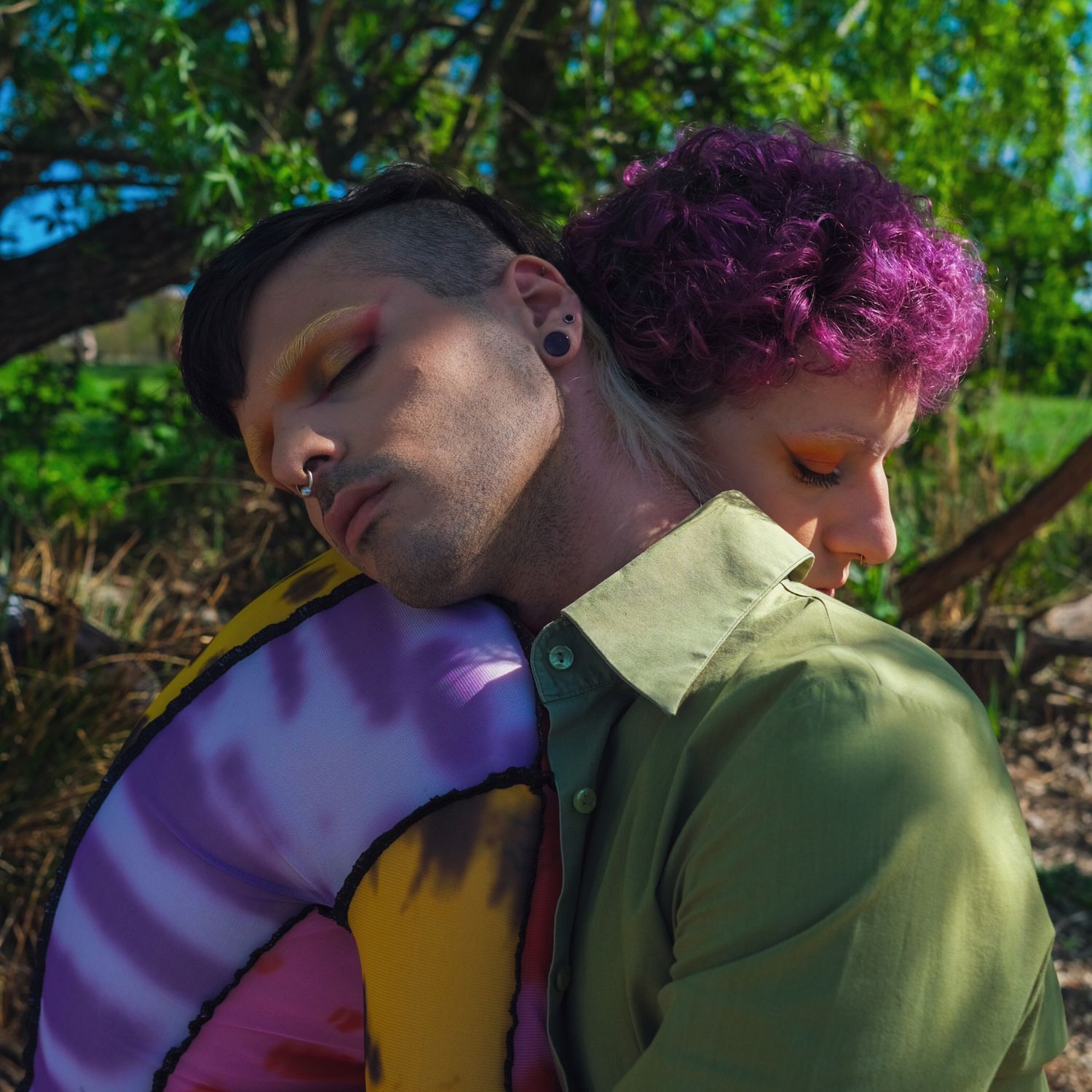 Two people leaning together outdoors, one with purple hair