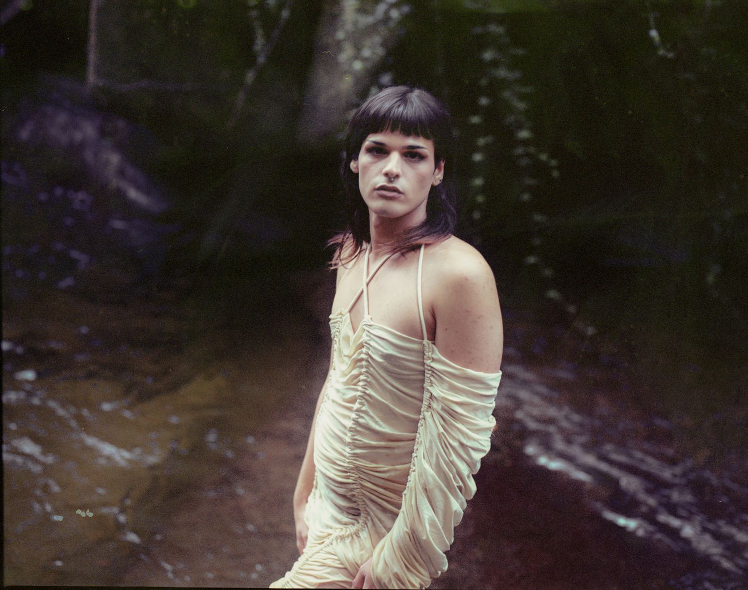 A person in a cream draped dress standing in a stream
