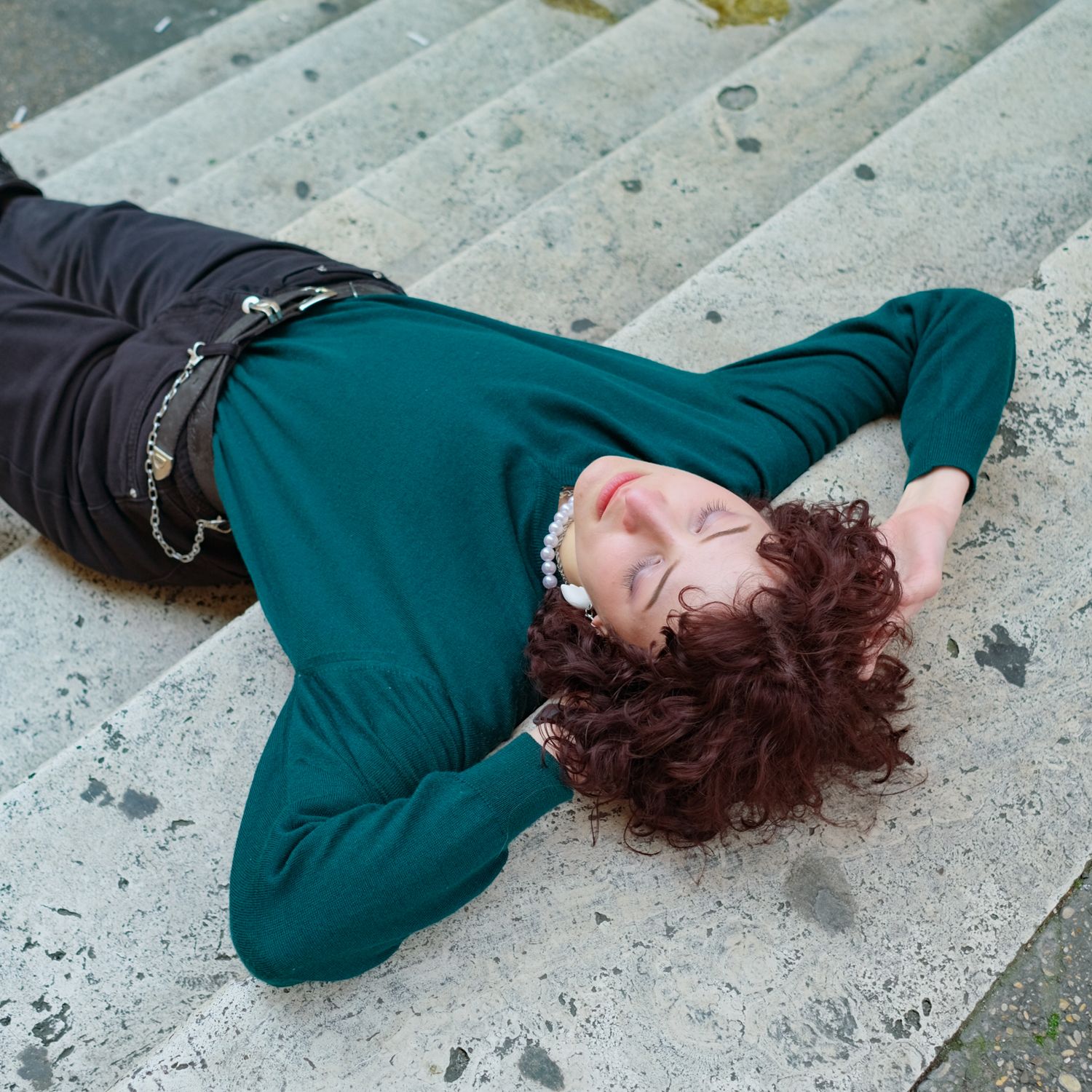 A person lying on stone steps, eyes closed, in a green sweater