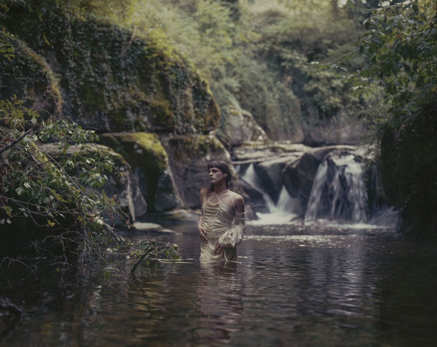 A person standing in a pool at the foot of a small waterfall